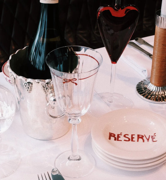 Wine glass with bow illustration around the rim on a table with white cloth and plates
