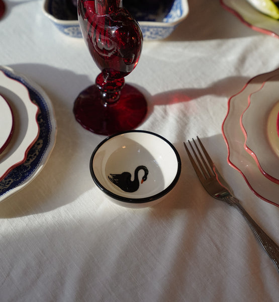Small ceramic tapas bowl with black swan in the middle on a tale set with plates on a white table cloth. 
