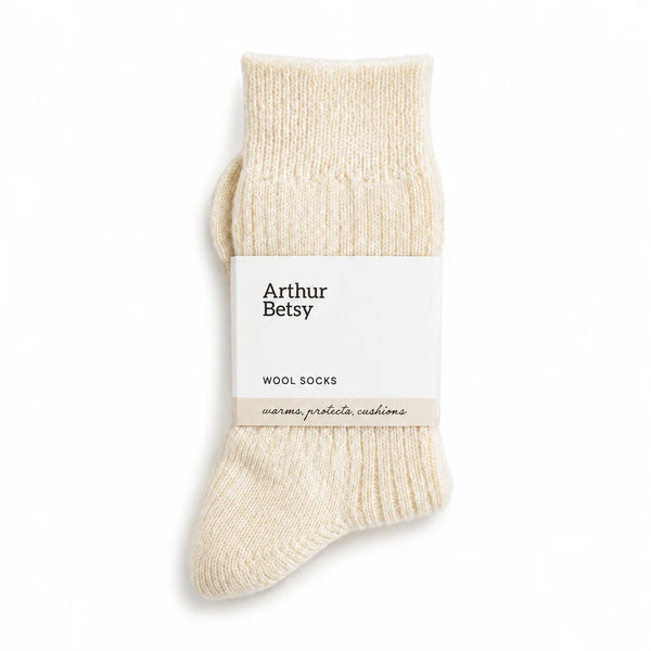 A pair of cream-colored knit wool socks with a white paper band label that reads 'Arthur Betsy WOOL SOCKS', shown on a clean white background.
