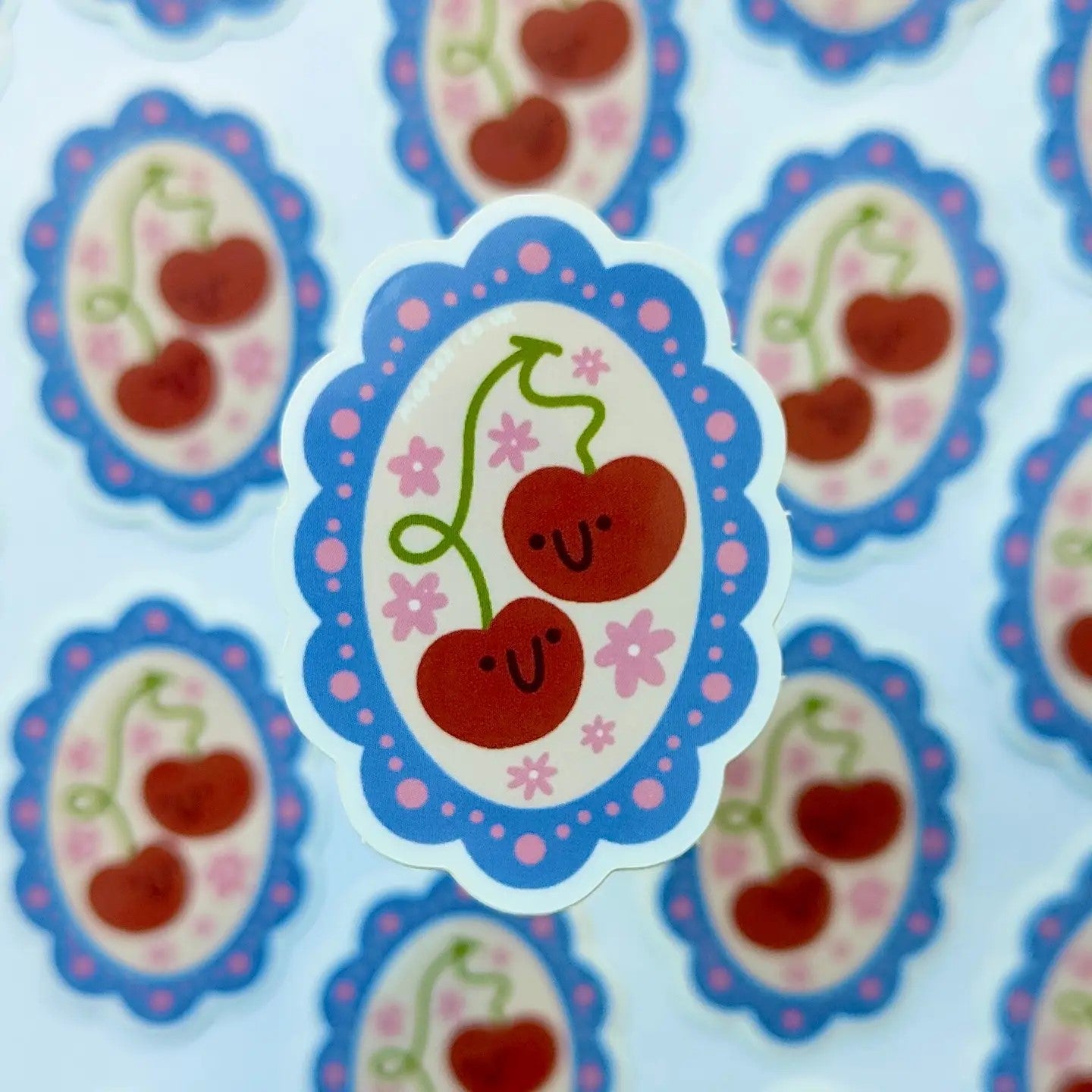 Sticker with cherries and a smiley face on a blue and pink background