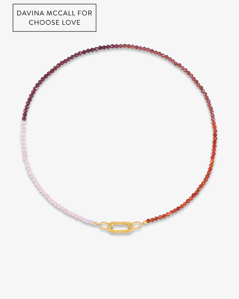 A beaded necklace with a gradient transition from pale pink on one side to deep burgundy red on the other, featuring a gold clasp and a gold brand plaque at the top left reading 'DAVINA MCCALL FOR CHOOSE LOVE'.