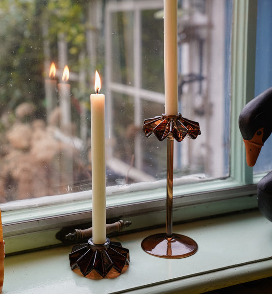 Decorative geometric candle holders with lit candles on a windowsill.
