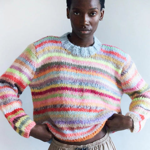 Person wearing a  hand knitted Dawn x Dare colourful striped sweater against a plain background