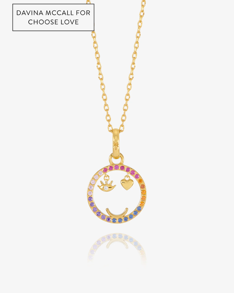 A gold chain necklace with a circular pendant featuring a smiley face design. The outer rim of the circle is lined with small multicolored stones in shades of pink, orange, yellow, and blue.