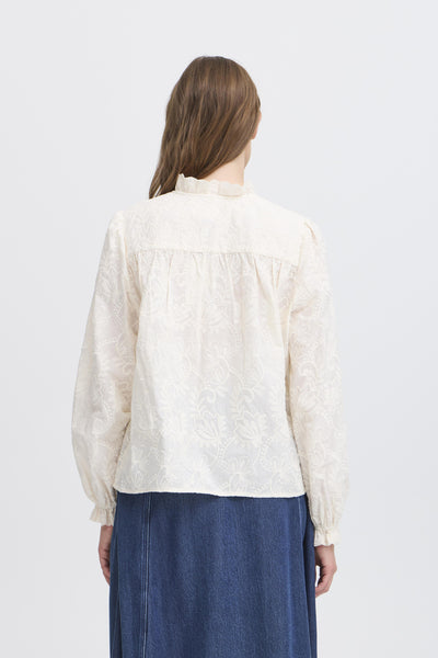 Person wearing a white  embroidered  blouse  with long sleeves view from the back. 