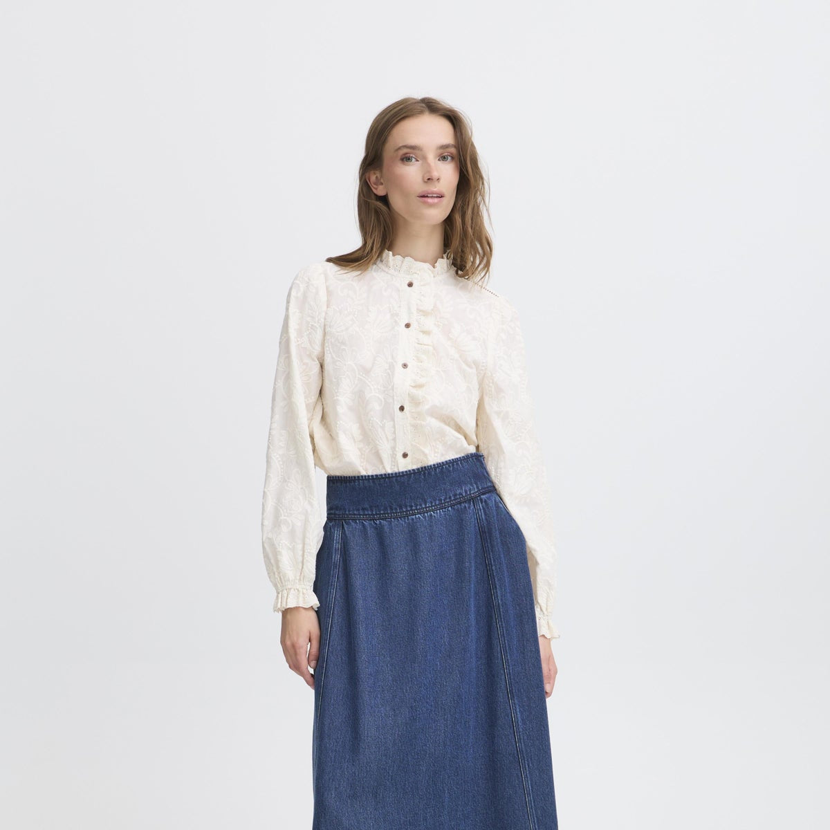 Woman wearing a white embroidered blouse, blue denim skirt.