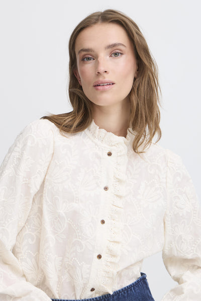 Woman wearing a white embroidered blouse with frill details 
