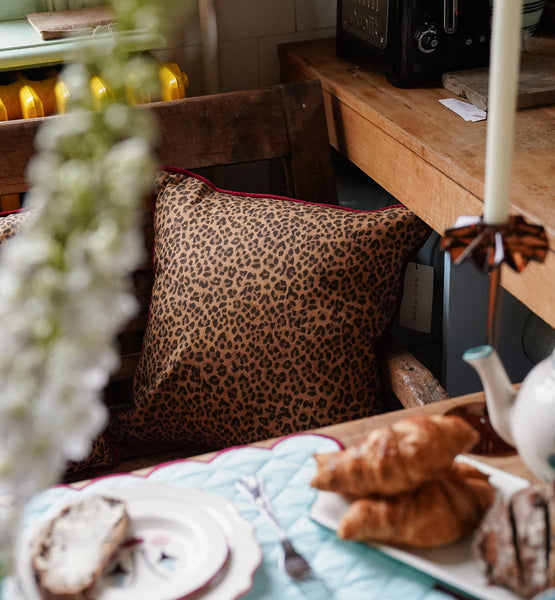 Leopard print cushion with red trimming  on a wooden chair 