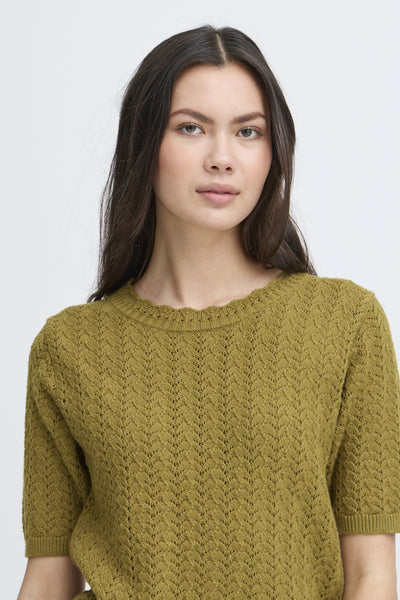Woman wearing green knitted sweater with short sleeves against a plain background
