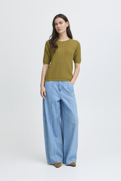 Woman wearing a green short sleeved sweater and blue pants on a white background