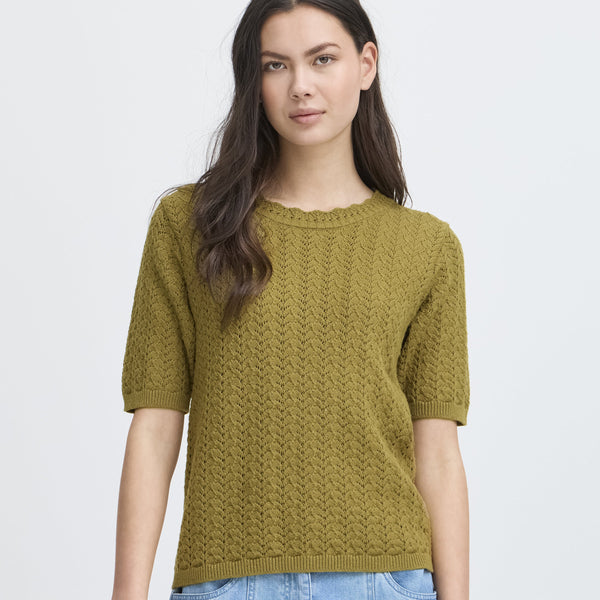 Woman wearing a green knitted short sleeved  sweater and blue jeans on a white background