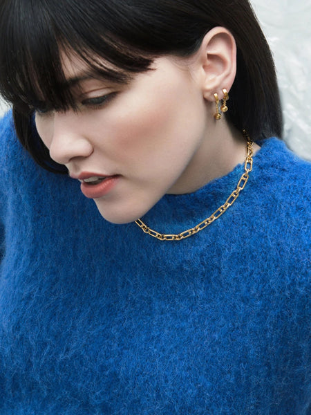 Woman wearing gold chunky necklace and blue jumper