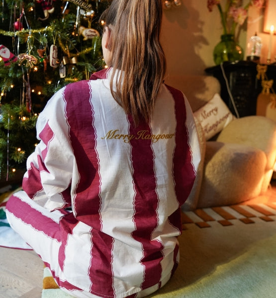 Person wearing a red and white striped shirt with 'Merry Hangover' text, sitting in a festive room with a Christmas tree.