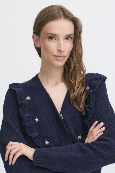 Woman wearing a navy blue cardigan with floral details. 