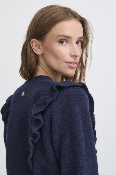 Woman wearing a navy blue cardigan with ruffled shoulders on a white background