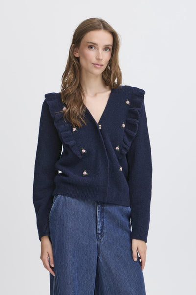 Woman wearing a navy blue cardigan with ruffled details and blue jeans on a white background