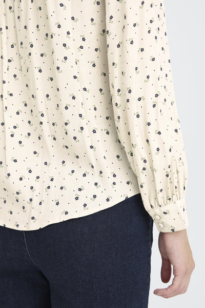 Close-up of a person wearing a cream blouse with black floral pattern. 