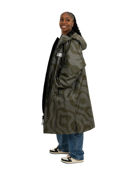 Person showing a camo green changing robe from the side with hand in pockets standing with a white background