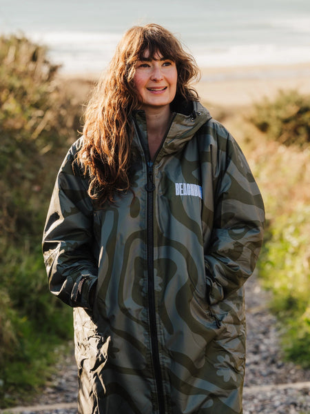Person in a green camo changing robe standing on a path near the sea