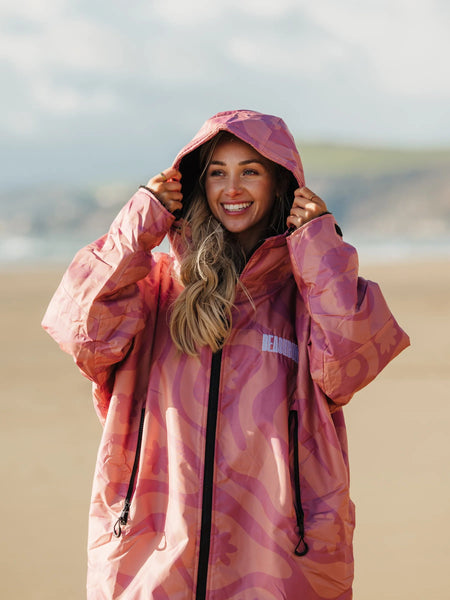 Woman wearing a pink camo changing robe with hood up on the beach. 