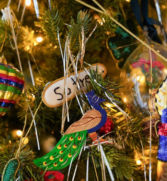 Decorative peacock ornament on a Christmas tree with other ornaments and lights.