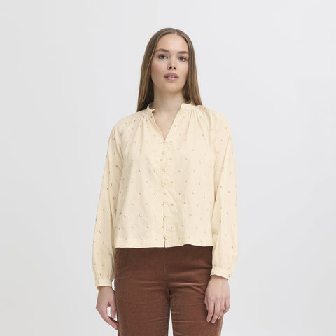 Woman wearing a beige blouse with repeat pattern and brown pants on a white background