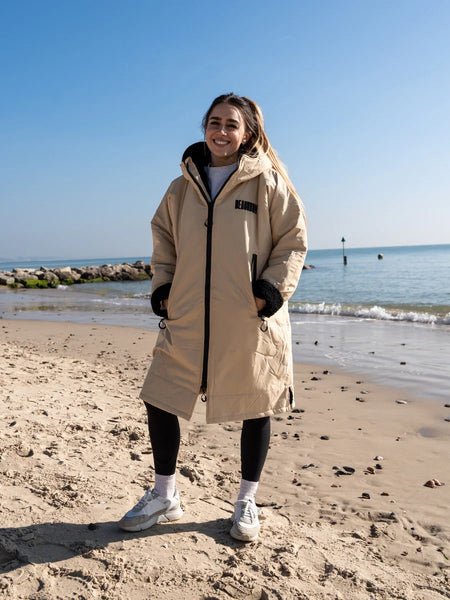 Person wearing a beige robe coat on a beach with ocean and clear sky in the background
