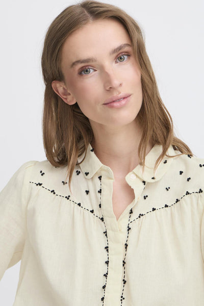 Woman wearing a cream-colored blouse with pan collar featuring black embroidery details