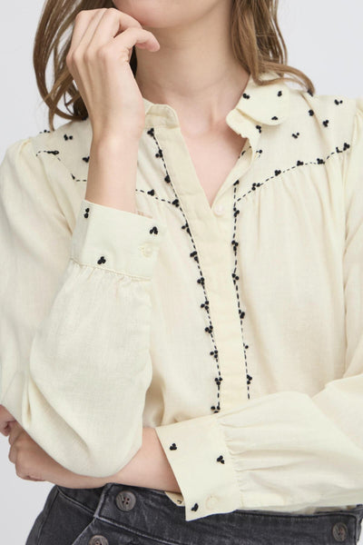 Close-up of a person wearing a cream-colored blouse with black details on a white background
