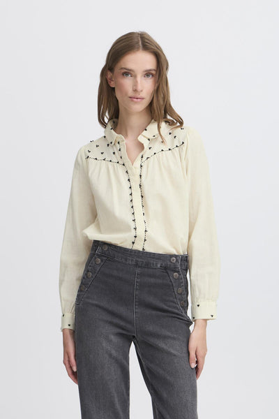 Woman wearing a cream blouse with black embroidery
