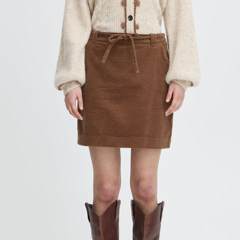 Person wearing a brown corduroy skirt and brown knee-high boots on a white background