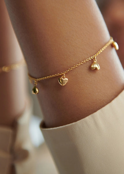 Gold bracelet with heart charms on a persons wrist